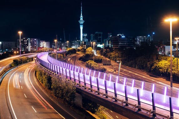 Evening view of Te Ara I Whiti, Pink Light Path from afar lit up with the sky tower in the background